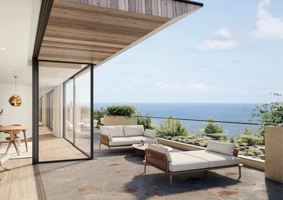 A covered balcony terrace with outdoor sofas, looking out over planted slopes to the sea