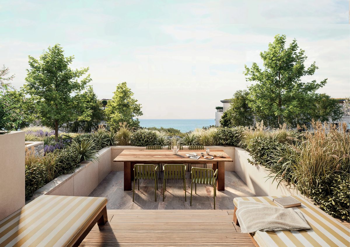 A sunken garden terrace with a dining table and loungers, with the sea beyond